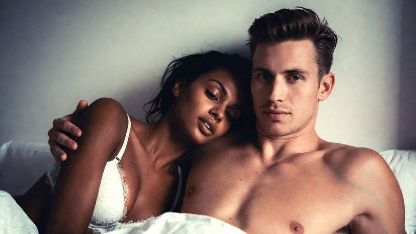 N&aelig;rbillede af et intimt, afkl&aelig;dt par i sengen, der kigger p&aring; kameraet.