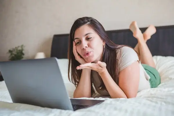 Kvinde flirter under sexchat på bærbar computer, liggende på seng, online sexdate og sex contact site kommunikation