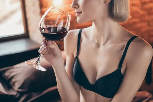 En kvinde i bh holder et glas rødvin i hånden og sætter det op til næsen.
